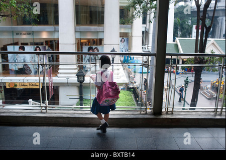 Schoolgirl sul marciapiede ha uno snack e guarda al centro commerciale moderno all'incrocio Ratchaprasong in Bangkok. Foto Stock