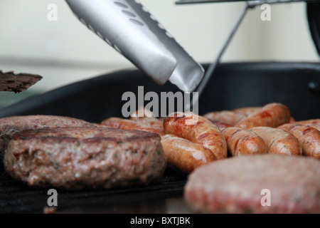 Primo piano di salsicce e hamburger essendo cotti su una piastra riscaldante a barbecue Foto Stock