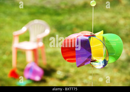 Kid giocattoli sparsi intorno sull'erba nel cortile con la girandola colorata Wind toy in primo piano. Foto Stock