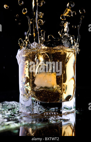 Bicchiere di whiskey su uno sfondo nero. Whiskey splash in un bicchiere. Il whiskey con ghiaccio. Foto Stock