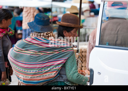 Signora boliviana in abito tradizionale con un giovane bambino in imbracatura sulla sua schiena, Huari, Bolivia, Sud America. Foto Stock