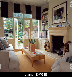 Ampia-nero rigato+persiane bianche sulle finestre alla francese con vista del giardino in crema stanza vivente con vasi di cactus sul caffè-tabella Foto Stock