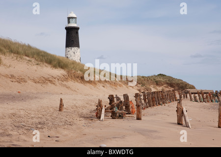 La spiaggia a disprezzare il punto che mostra il faro e le difese del mare Foto Stock