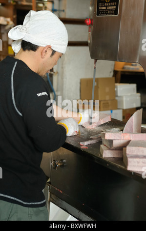 Lavoratore giapponese il taglio di tonno congelato in pezzi con sega elettrica, il Mercato del Pesce di Tsukiji, Tokyo, Giappone Foto Stock