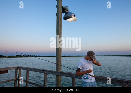 Stati Uniti d'America, in Texas, il Lago Arrow-parco statale, giovane uomo baci pesce per buona fortuna durante la pesca da pubblica il dock sulla serata estiva Foto Stock