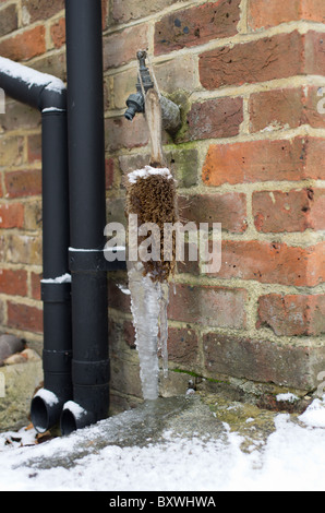 Grandi forme icicle su brush sotto un rubinetto che gocciola Foto Stock