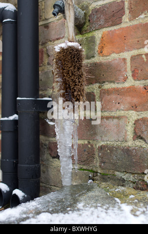 Grandi forme icicle su brush sotto un rubinetto che gocciola Foto Stock