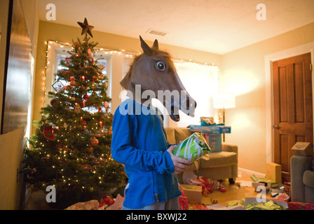 Un bambino che indossa una testa di cavallo maschera durante l'apertura in un regalo di Natale nel soggiorno il giorno di Natale. Foto Stock