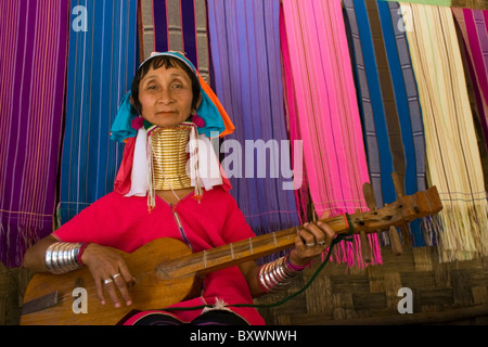 Un Karen Paduang giraffa rifugiato donna è seduta al di fuori di casa sua riproduzione di una chitarra di legno in Ban Nai Soi, Thailandia. Foto Stock