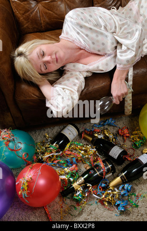 Donna che mantiene un vuoto di vetro del vino la posa su un divano e dormire per i postumi di una sbornia Foto Stock