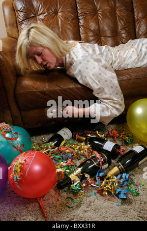 Donna che mantiene un vuoto di vetro del vino la posa su un divano e dormire per i postumi di una sbornia Foto Stock
