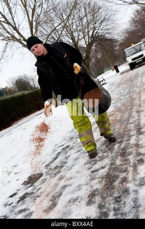 Autorità locale consiglio lavoratori graniglia di spandimento e sale a mano sul sentiero ghiacciato per una scuola, Wales UK Foto Stock