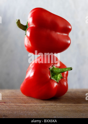 2 peperoni rossi bilanciato sulla parte superiore di ogni altro contro uno sfondo nero Foto Stock