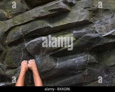 Una coppia di mani appeso ad un muro di pietra e rocciosa affiorante Foto Stock