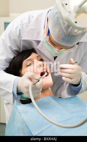 L'immagine verticale del paziente di sesso femminile con il dentista oltre il suo controllo su denti e li di perforazione Foto Stock