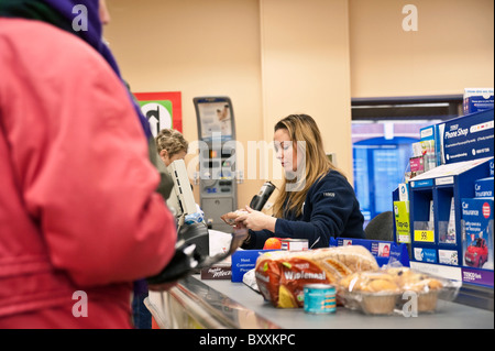 Check out operatore in un supermercato Tesco, UK. Cassa Cassa all'interno di un negozio. Articoli alimentari sul nastro trasportatore al momento del check out. Foto Stock