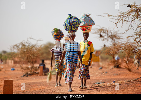 Donne che arrivano nella città di Djibo, Burkina Faso a piedi, portando la loro mercanzia sulle loro teste in tradizionale moda africana. Foto Stock