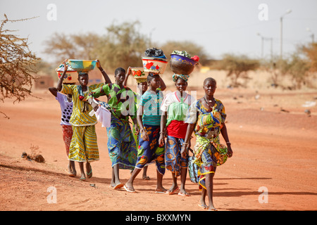 Donne che arrivano nella città di Djibo, Burkina Faso, a piedi, portando la loro mercanzia sulle loro teste in tradizionale moda africana. Foto Stock