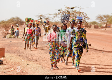 Donne che arrivano nella città di Djibo, Burkina Faso, a piedi, portando la loro mercanzia sulle loro teste in tradizionale moda africana. Foto Stock