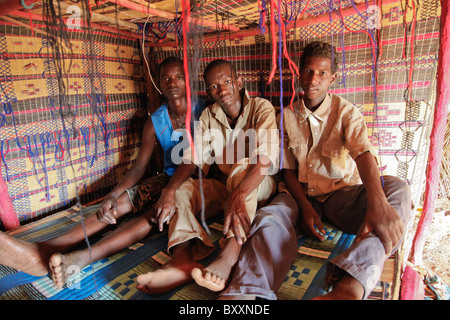 In Fulani villaggio di Jolooga nel nord del Burkina Faso, tre giovani uomini di sedersi su un letto tradizionale in una casa fatta di paglia. Foto Stock