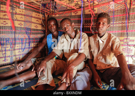 In Fulani villaggio di Jolooga nel nord del Burkina Faso, tre giovani uomini di sedersi su un letto tradizionale in una casa fatta di paglia. Foto Stock