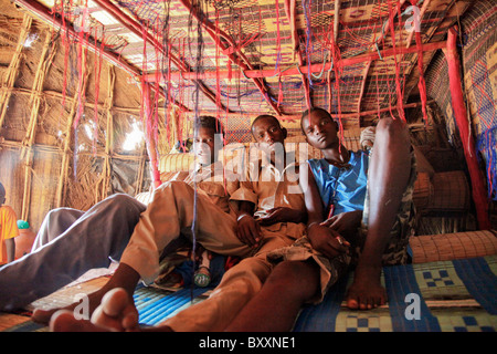 In Fulani villaggio di Jolooga nel nord del Burkina Faso, tre giovani uomini di sedersi su un letto tradizionale in una casa fatta di paglia. Foto Stock