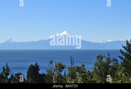 Cielo blu vista su alberi verdi e delle acque blu del Lago Llanquihue, guardando verso il cono di ghiaccio del Volcan Osorno, Cile Foto Stock