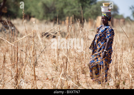 Una donna che trasporta merci sul suo capo del Villaggio Mercato di Bourro nel nord del Burkina Faso. Foto Stock