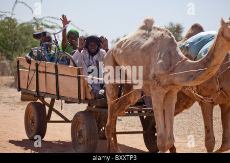 Un gruppo di Fulani cavalcare un cammello carrello attraverso il Villaggio Mercato di Bourro nel nord del Burkina Faso. Foto Stock