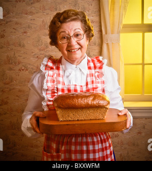 Un anziana senior citizen moglie contadino visualizza fresche fatte pagnotta di pane sul tagliere. La mattina presto la luce della finestra Foto Stock