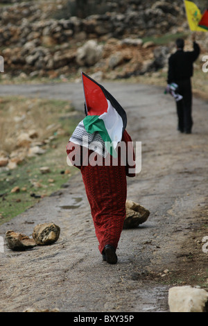 La donna palestinese cammina con la bandiera palestinese durante un rally settimanale contro la costruzione delle barriere di separazione controverse che Israele sta costruendo nel villaggio della Cisgiordania di Bil'in Israele Foto Stock