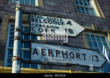 Indicazioni stradali in gaelico e inglese punto la direzione a Cork, l'aeroporto e Gelgooly nella contea di Cork, Irlanda Foto Stock