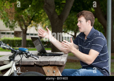 Venti-qualcosa maschio smorfie degli studenti su ciò che vede sullo schermo del proprio computer Foto Stock