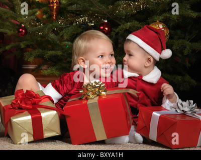 Due anno vecchia ragazza e un ottavo mese old boy condivisione dei doni sotto un albero di Natale Foto Stock