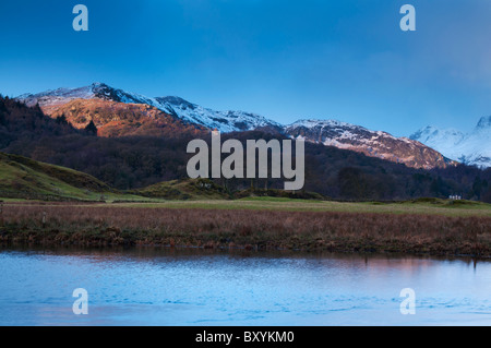 Il sole illumina la neve e rabboccato fells a Elterwater nella grande Langdale Valley, Lake District Foto Stock