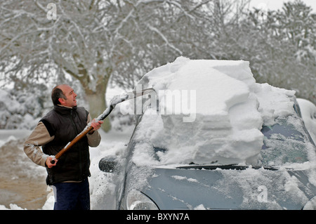 Un uomo si cancella la neve dalla sua auto. Foto Stock