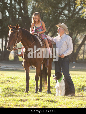 L'uomo anziano con il cane ad assistere la nipote passeggiate a cavallo nel ranch Foto Stock