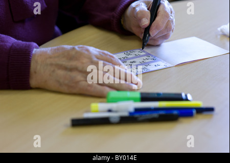 Chiudere l immagine della signora anziana con le mani in mano la marcatura la sua scheda di bingo sulla scrivania con un numero di penne nelle vicinanze. Foto Stock