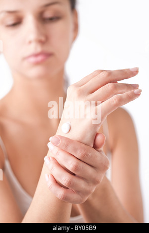 Sorridente giovane donna si applica la crema sulle mani. Su uno sfondo bianco. Foto Stock