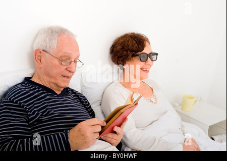 Coppia senior in bed uomo donna lettura guardando la TV 3D con occhiali speciali Foto Stock