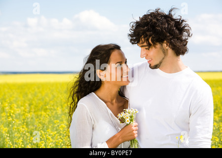 Ritratto di bella ragazza con mazzo di chamomiles con bello guy standing vicino mentre sia guardando ogni altra smili Foto Stock