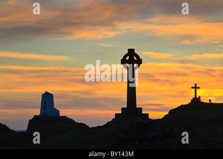 St Dwynwen croce celtica e Twr Mawr faro in silhouette sull isola di Llanddwyn al tramonto Isola di Anglesey, Galles del Nord, Regno Unito Foto Stock