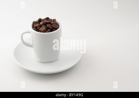 Una tazza di espresso riempito con i chicchi di caffè si siede su un piattino. Fotografati contro uno sfondo neutro. Foto Stock