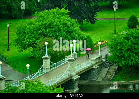 Donna che cammina da sola sotto la pioggia sul ponte sulla laguna in Boston Public Garden. Foto Stock