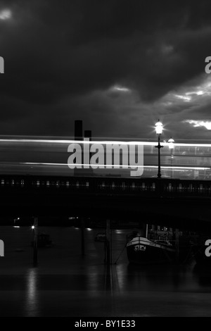 London bus passando sul ponte di Battersea, a Chelsea, Londra, Regno Unito. I vecchi lotti su strada la stazione di alimentazione può essere visto in lontananza. Foto Stock