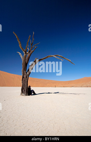 La Namibia, Deadvlei. Un turista trova una spec di ombra sotto uno degli antichi alberi morti di Deadvlei. Foto Stock