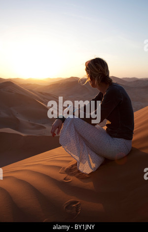 Oman, Empty Quarter. Una giovane donna orologi il Sun andare giù sopra le dune. Il sig. Foto Stock