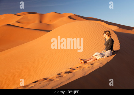 Oman, Empty Quarter. Una giovane donna orologi il Sun andare giù sopra le dune. Il sig. Foto Stock