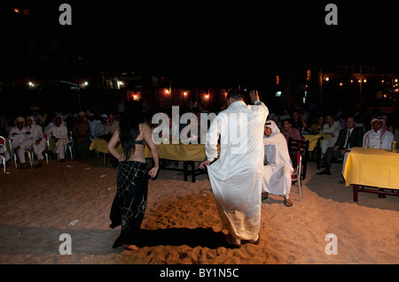 Gli uomini frequentano beduino tradizionale celebrazione dei matrimoni danza professionale con una danzatrice del ventre da Beirut come lei intrattiene gli ospiti. Foto Stock