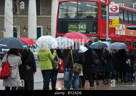 In una coda di attesa di persone sotto la pioggia a bordo di una red London bus Foto Stock